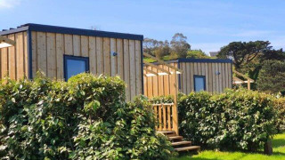 Outdoor view of Cottage Prestige cabins with wooden exterior, green hedges, and a clear blue sky.
