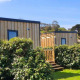 Udendørs foto af Cottage Prestige-træhytter med grønne hække og blå himmel i baggrunden.