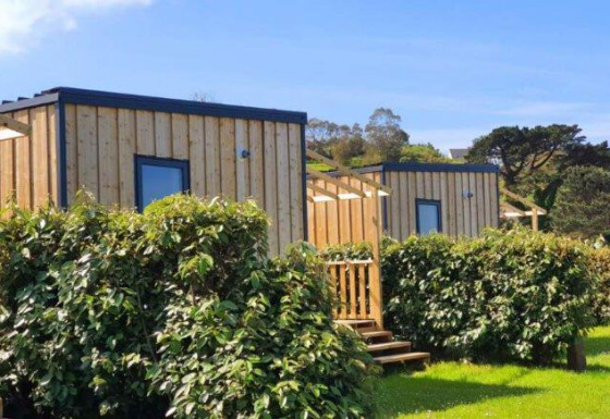 Udendørs foto af Cottage Prestige-træhytter med grønne hække og blå himmel i baggrunden.