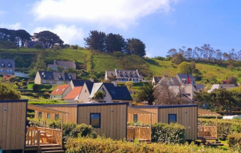 Cabañas Cottage Prestige en Camping Seasonova Les 7 Iles, Francia, rodeadas de colinas verdes y casas rurales.