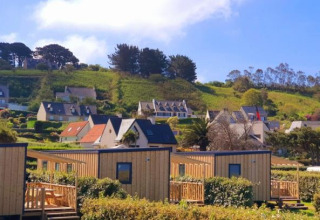 Cabañas Cottage Prestige en Camping Seasonova Les 7 Iles, Francia, rodeadas de colinas verdes y casas rurales.