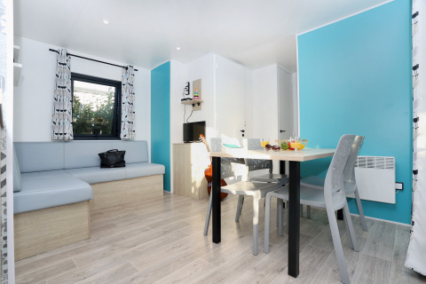 Moderne opholdsstue i Cottage Prestige på Camping Seasonova Les 7 Iles med blå vægge og spisebord.