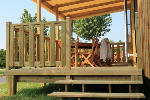 Porche de madera con mesa y sillas en Cottage Prestige, Camping Seasonova Les 7 Iles, Francia.
