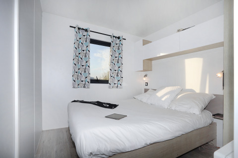 Modernes, helles Schlafzimmer im Cottage Prestige bei Camping Seasonova Les 7 Iles in Frankreich mit Doppelbett.