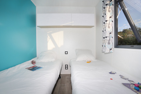 Two single beds with white bedding in a bright room with a blue accent wall and window at Cottage Prestige cabin.