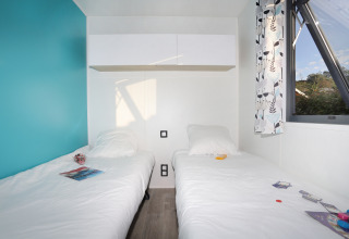 Two single beds with white bedding in a bright room with a blue accent wall and window at Cottage Prestige cabin.