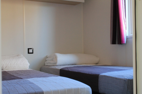 Two single beds with simple bedding in a bright room at Cottage Prestige, Camping Seasonova Les 7 Iles, France.