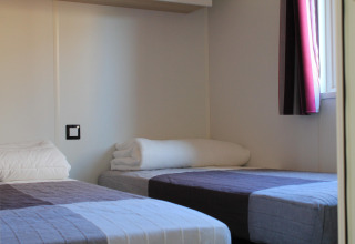 Two single beds with simple bedding in a bright room at Cottage Prestige, Camping Seasonova Les 7 Iles, France.