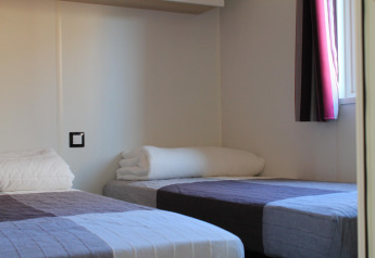 Two single beds with simple bedding in a bright room at Cottage Prestige, Camping Seasonova Les 7 Iles, France.
