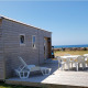 En lille træhus kaldet Tiny House med terrasse, havudsigt og havemøbler under en klar blå himmel.