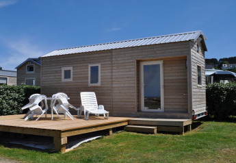 Una pequeña casa de madera con terraza y sillas blancas en Camping Seasonova Les 7 Iles, Francia.