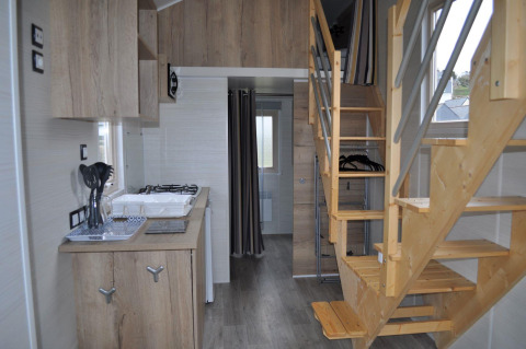 Interior view of a tiny house at Camping Seasonova Les 7 Iles, featuring a wooden staircase and compact kitchen.