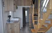 Interior view of a tiny house at Camping Seasonova Les 7 Iles, featuring a wooden staircase and compact kitchen.