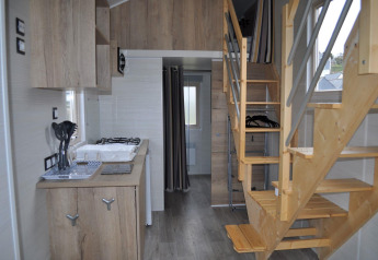 Interior view of a tiny house at Camping Seasonova Les 7 Iles, featuring a wooden staircase and compact kitchen.