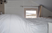 Interior view of a tiny house with a bed and window facing the beach at Camping Seasonova Les 7 Iles, France.