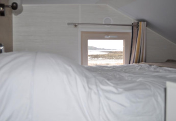 Interior view of a tiny house with a bed and window facing the beach at Camping Seasonova Les 7 Iles, France.