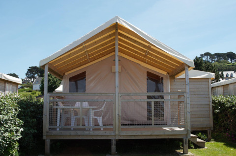 Eco Lodge cabin with wooden frame, covered front porch, and white chairs, surrounded by greenery outdoors.