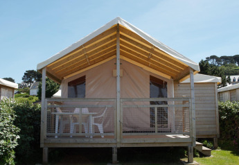 Eco Lodge cabin with wooden frame, covered front porch, and white chairs, surrounded by greenery outdoors.