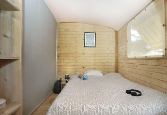 Cozy wooden cabin interior at Eco Lodge, Camping Seasonova Les 7 Iles, France, with a bed and decor.