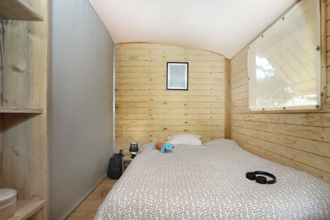 Intérieur de cabane en bois à l’Eco Lodge, Camping Seasonova Les 7 Iles, France, avec lit et déco.