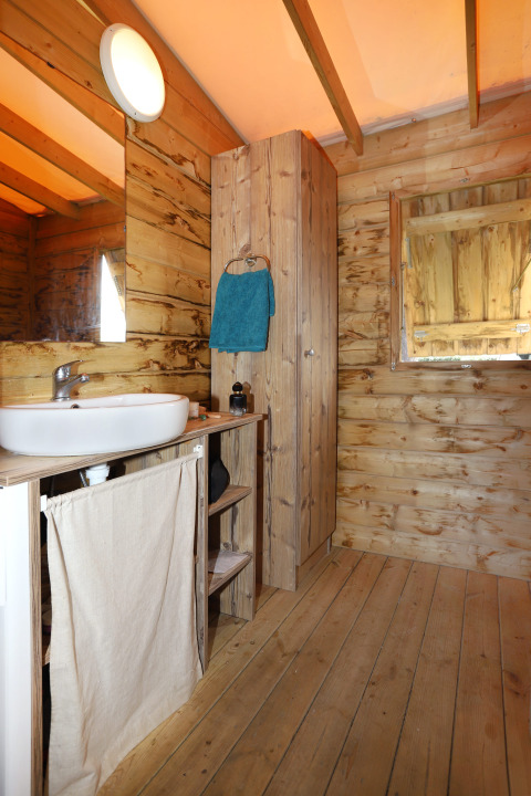 Baño rústico de madera con lavabo y toalla azul en Eco Lodge, Camping Seasonova Les 7 Iles, Francia.