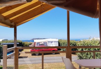 View from an Eco Lodge cabin at Camping Seasonova Les 7 Îles in France showing caravans, hedges, and sea.