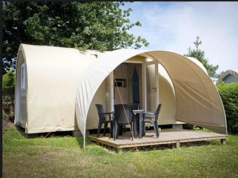 Tenda safari Coco Sweet con terrazza, mobili da giardino e porta aperta, immersa nel verde degli alberi.