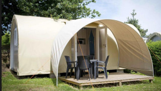 Tenda safari Coco Sweet con terrazza, mobili da giardino e porta aperta, immersa nel verde degli alberi.