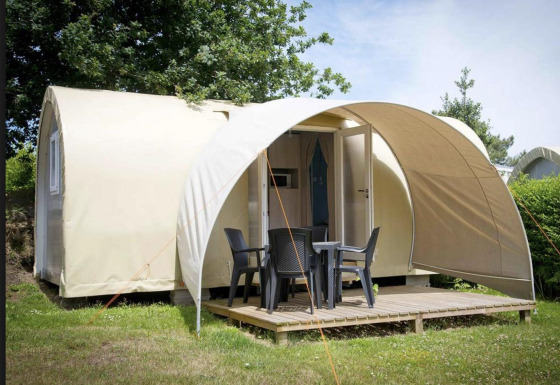 Coco Sweet safari tent with wooden terrace, patio chairs and table, surrounded by greenery and trees.