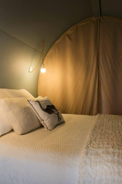 Indvendig udsigt af en hyggelig safari-telt Coco Sweet med seng og lamper på Camping Seasonova Les 7 Iles i Frankrig.