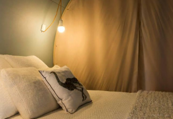 Vista interna di una tenda safari Coco Sweet con letto e lampade al Camping Seasonova Les 7 Iles in Francia.