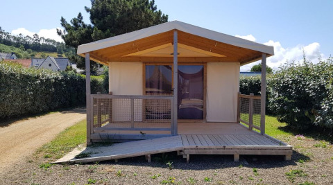 Cabaña Ecolodge Pmr con rampa de madera y porche, rodeada de vegetación y setos bajo el sol.