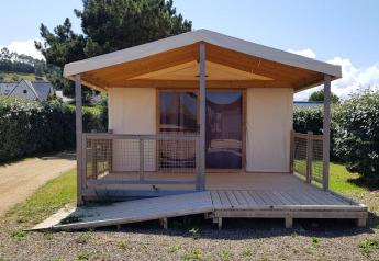 Ecolodge Pmr kabine med rampe og træterrasse, omgivet af grønne hække under en blå himmel.