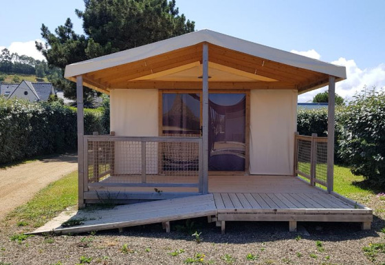 Cabaña Ecolodge Pmr con rampa de madera y porche, rodeada de vegetación y setos bajo el sol.