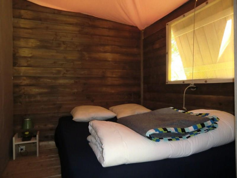 Acogedor dormitorio con paredes de madera, cama y ventana en Ecolodge Pmr, Camping Seasonova Les 7 Iles, Francia.