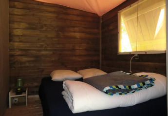 Hyggeligt soverum med trævægge, seng og vindue i Ecolodge Pmr på Camping Seasonova Les 7 Iles i Frankrig.