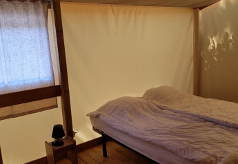 Camera da letto nell’Ecolodge PMR al Camping Seasonova Les 7 Iles, Francia, con letto e arredi in legno.