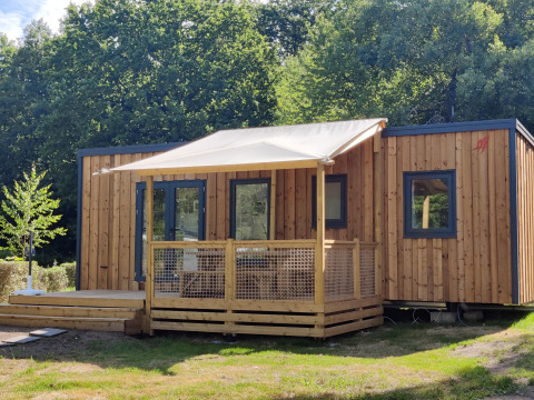 Modern Cottage Prestige chalet with wood siding, shaded veranda, and surrounded by greenery and trees.