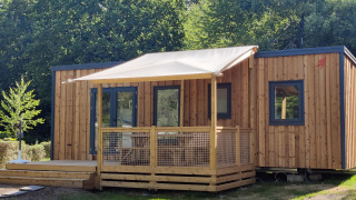 Chalet moderno Cottage Prestige in legno con veranda ombreggiata, immerso nel verde e circondato da alberi.
