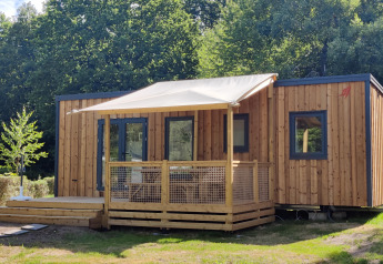 Chalet moderno Cottage Prestige in legno con veranda ombreggiata, immerso nel verde e circondato da alberi.