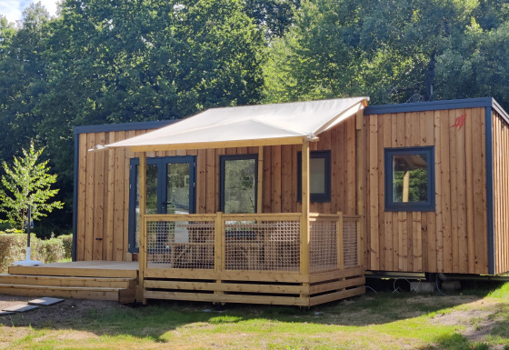 Modern Cottage Prestige chalet with wood siding, shaded veranda, and surrounded by greenery and trees.