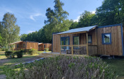 Foto del Cottage Prestige en Camping Seasonova Les Vosges du Nord con cabañas de madera y vegetación.