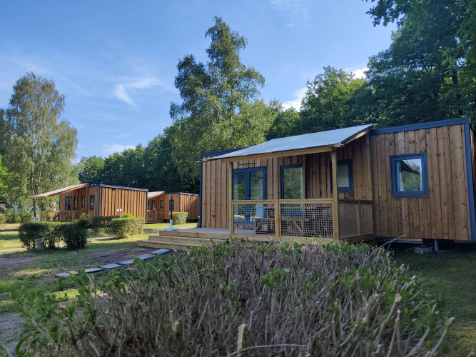 Foto del Cottage Prestige en Camping Seasonova Les Vosges du Nord con cabañas de madera y vegetación.