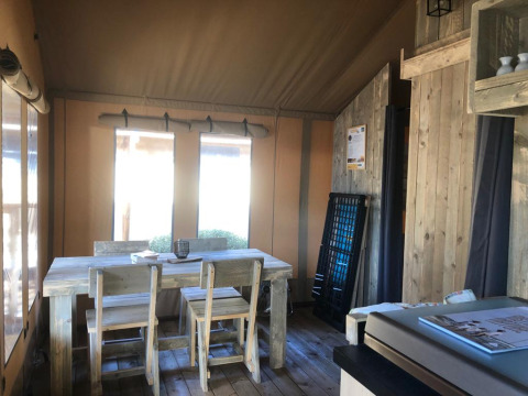 Vista interior de una tienda safari con mesa de comedor de madera rústica, sillas y suave iluminación.