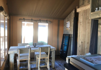Vista interior de una tienda safari con mesa de comedor de madera rústica, sillas y suave iluminación.