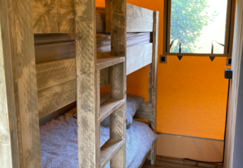 Pequeño dormitorio en una tienda safari con literas de madera, suelo de madera y ventana con vista.