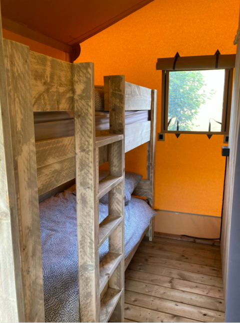 Small sleeping area inside a safari tent, featuring a wooden bunk bed, wood floor, and a window view.