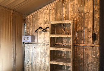 Safari tent interior with wooden shelves, clothes hangers, and safe, set against rustic wooden walls.