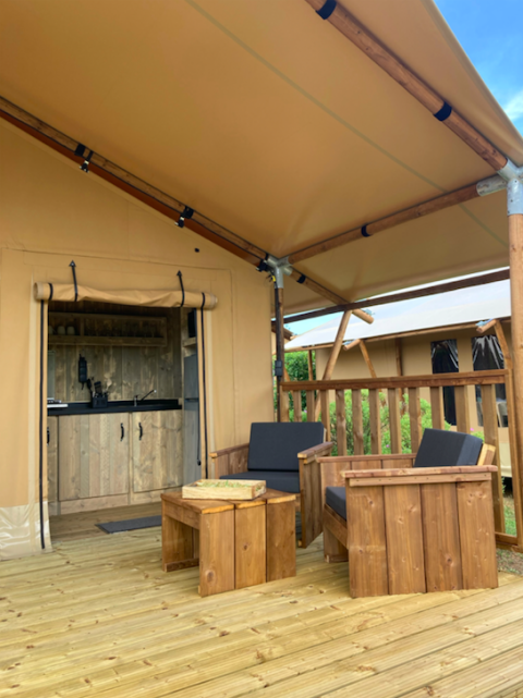 Wooden deck with cushioned chairs and table outside a safari tent featuring a small kitchenette.