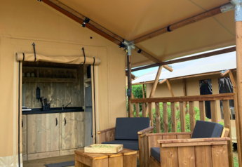 Wooden deck with cushioned chairs and table outside a safari tent featuring a small kitchenette.